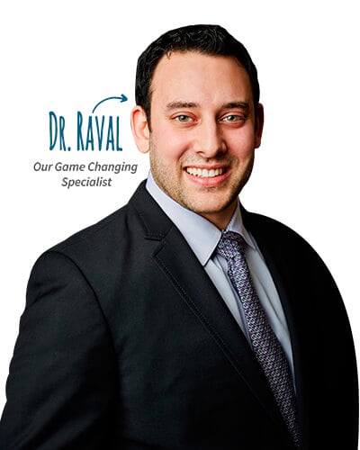 Dr. Neal Raval, our game changing specialists, standing and smiling while wearing a black suit.