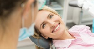A woman sitting in dental chair and looking up at dentist.